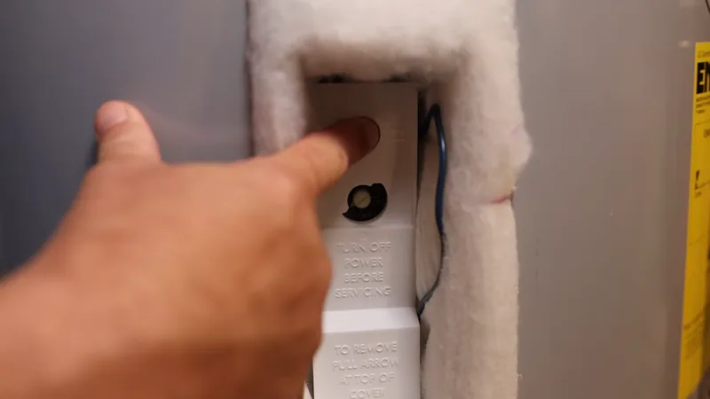 Technician pressing the red high-limit reset button on an electric water heater thermostat panel